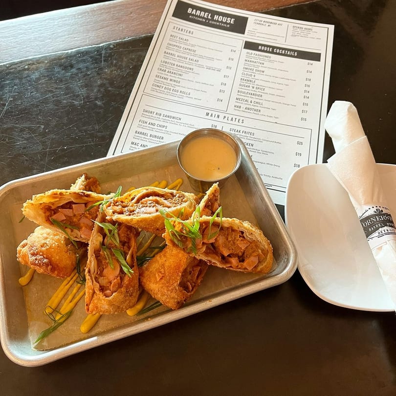 Barrel House Coney Dog Egg Rolls with dipping sauce on a metal tray next to a menu.
